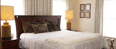 A neatly made bed with a white duvet and multiple pillows, flanked by two bedside tables with lamps, in a room with wooden paneling and framed pictures on the wall.
