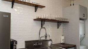 Una cocina con un lavamanos de acero inoxidable, repisas de madera y salpicadero de azulejos blancos.