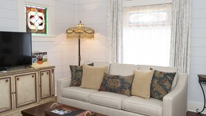 Una sala de estar con un sofá, un televisor, una lámpara y un ventanal con cortinas.