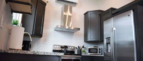 A modern kitchen with dark cabinetry, stainless steel appliances, a built-in oven, microwave, and a refrigerator.
