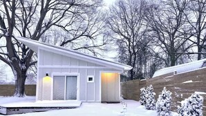A modern house with a white exterior, a wooden deck, and a snow-covered yard. - Modern guesthouse in downtown TR (Travelers Rest)