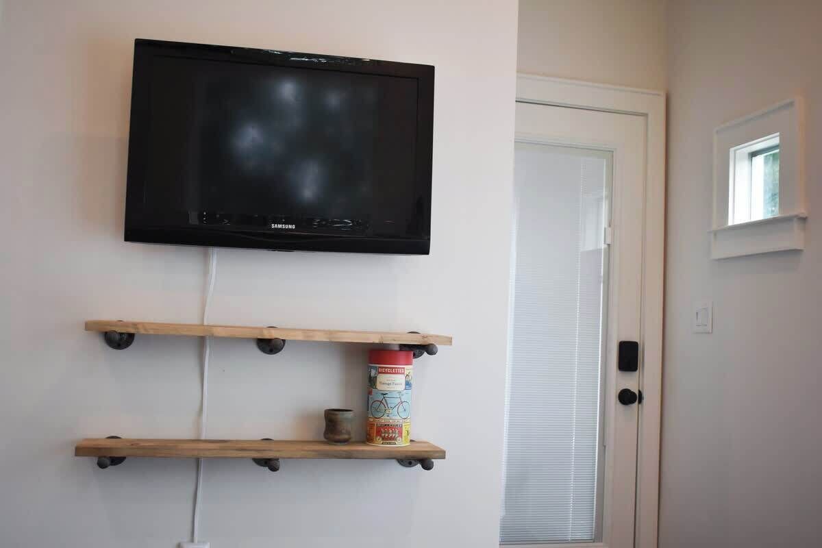 Ein an der Wand befestigtes Fernsehgerät über einem Holzregal mit einer Bierdose und einem kleinen Topf.