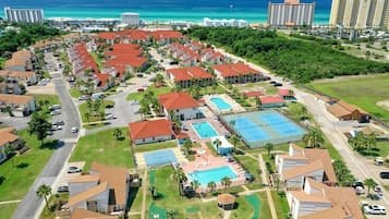 Um resort com vários edifícios, piscina, quadras de tênis e vista para o oceano.