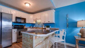 Una cucina con mobili bianchi, un frigorifero in acciaio inossidabile, un forno a microonde e un'isola in legno con sgabelli da bar.