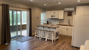 A modern kitchen with white cabinets, a central island with stools, a microwave, and a refrigerator. - River View Loft on the Mermentau River with pool access (Mermentau)