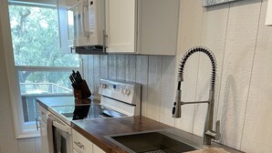 A modern kitchen with white cabinetry, a wooden countertop, a stainless steel sink, and a built-in oven. - River View Loft on the Mermentau River with pool access (Mermentau)