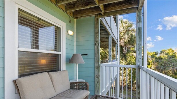 A porch with a wicker sofa, a table with a lamp, and a view of trees and sky. - Nature's Landing - A102 Budget Rates Downtown Unit (Cedar Key)
