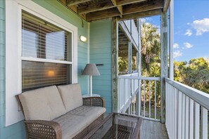 A porch with a wicker sofa, a table with a lamp, and a view of trees and sky. - Nature's Landing - A102 Budget Rates Downtown Unit (Cedar Key)