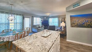 A living room with a dining area, a kitchen island, and a painting on the wall. - Nature's Landing A104 Prettiest Condo in Town! (Cedar Key)