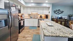 A modern kitchen with white cabinets, a granite countertop, and a stainless steel refrigerator. - Nature's Landing A104 Prettiest Condo in Town! (Cedar Key)