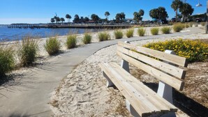 A sandy beach with a wooden bench and a concrete walkway. - Nature's Landing A104 Prettiest Condo in Town! (Cedar Key)