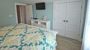 Um quarto com cama, televisão na parede, guarda-roupa branco e uma porta.