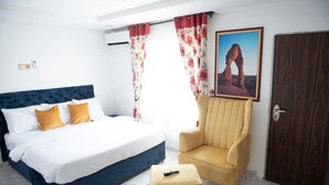 Quarto com cama, uma cadeira, controle remoto e uma porta.