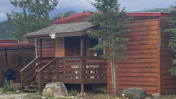 Un chalet rustique en bois, doté d’un escalier menant à un balcon, et entouré d’un paysage naturel.