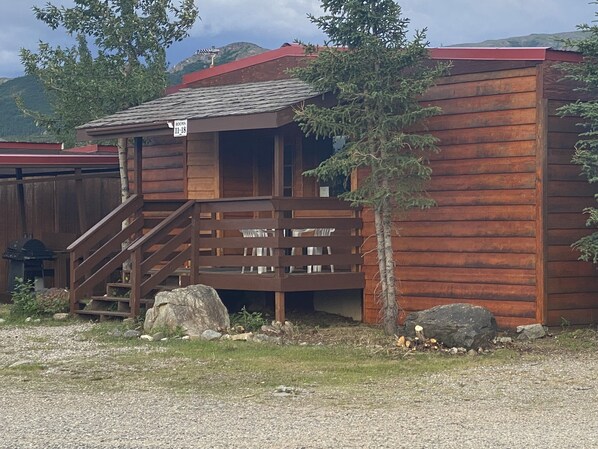 A rustic wooden cabin with a staircase leading to a balcony, surrounded by natural scenery. - Denali RV Park and Motel (Healy)