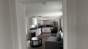 A modern kitchen with white cabinets, a refrigerator, and a microwave. There is a dining area with a table and chairs. - Beach Ave Escape Unit B - Just steps from the Beach! (Redington Shores)