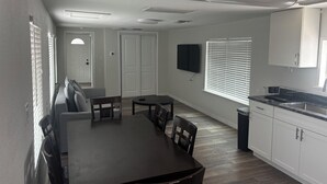 A dining area with a table and chairs, a kitchen with white cabinets, a window with blinds, and a ceiling fan. - Beach Ave Escape Unit B - Just steps from the Beach! (Redington Shores)