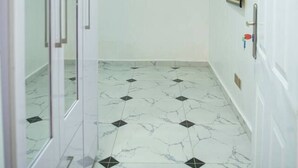 A hallway with white walls, a tiled floor, and a door with a handle. - Lovely One-bed Apartment Located in Abuja (Abuja)