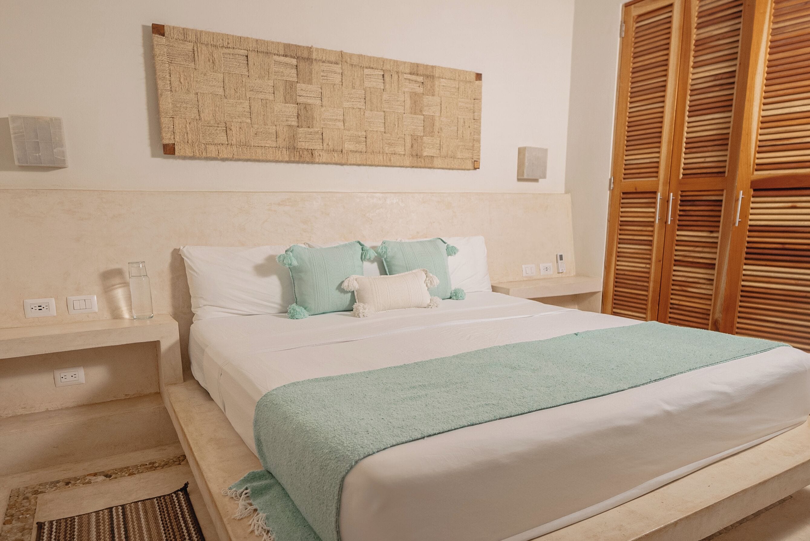Una camera da letto ordinata con un letto, comodini, un arazzo tessuto e persiane in legno.