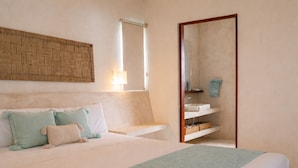 A bedroom with a bed, a bedside table, a mirror, and a built-in shelf with toiletries. - Casa Astral Hotel Boutique and Apartments (Isla Holbox)