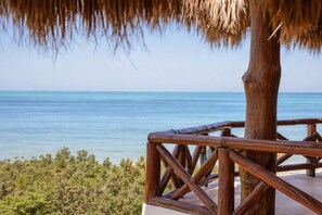 A wooden deck with a thatched roof overlooking a clear blue sea.
