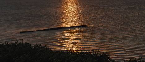 A sunset over the ocean with a calm sea and a distant landmass.