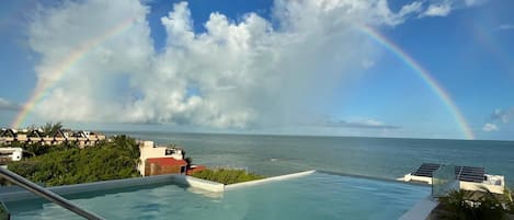 A infinity pool with a view of the ocean and a rainbow.