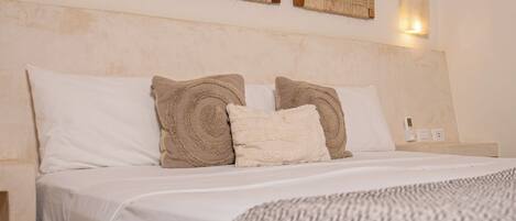 A neatly made bed with white and beige pillows, a patterned throw blanket, and a wall-mounted light fixture.