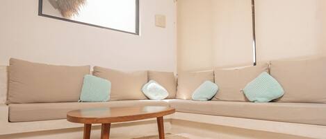 A living room with a beige sofa, a wooden coffee table, and a large window with a view of a tree.