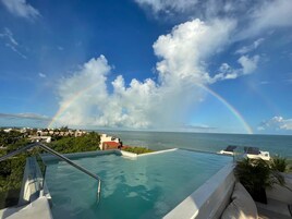 Una piscina infinita con vista al océano y un arcoíris.