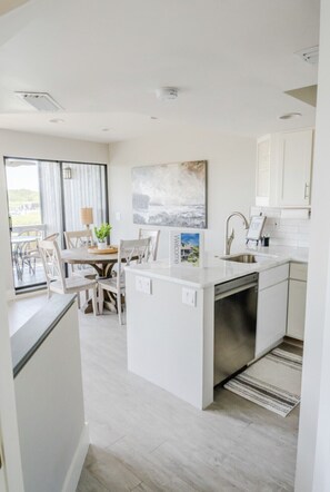 A modern kitchen with white cabinets, a built-in dishwasher, and a dining area with a round table and chairs.