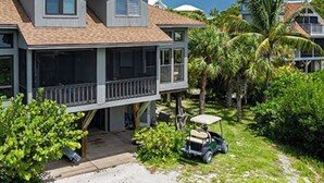 A two-story house with a balcony, surrounded by greenery and a golf cart. - CaptiVista! Your dream waterfront escape! Rustic luxury with unbelievable views! (North Captiva Island)
