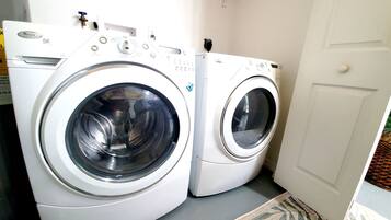 To frontindlæsende Whirlpool Duet vaskemaskiner i et vaskerum med gråt gulv og hvid dør.
