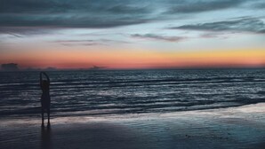 A beach with a silhouette of a person standing on the sand, facing the ocean.