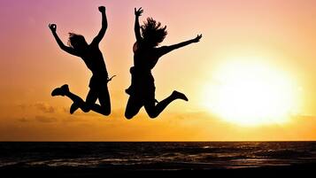 Two silhouetted figures jumping against a sunset over the ocean.