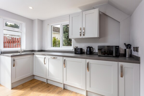 A modern kitchen with white cabinets, a wooden countertop, and a window with a view of greenery outside.