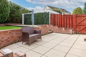 A patio area with a wicker chair, brick walls, and a red gate. - Leeward House - Donnini Apartments (Ayr)