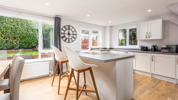 Una cocina moderna con una isla central, armarios blancos y un ventanal con vistas a un jardín.