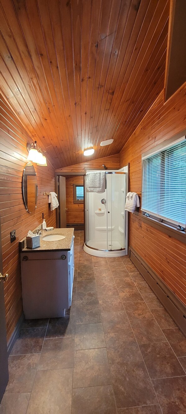 Un baño con paneles de madera, un lavabo, un espejo y una ducha.