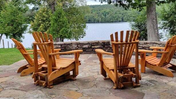 Une terrasse en pierre avec des fauteuils Adirondack donnant sur un lac.