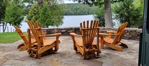 Une terrasse en pierre avec des fauteuils Adirondack donnant sur un lac.