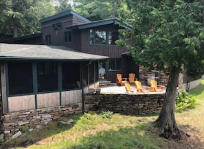 A two-story house with a stone foundation and a covered patio area with Adirondack chairs.