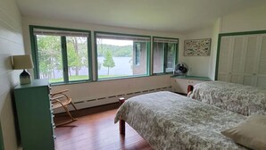 Une chambre avec deux lits, un fauteuil à bascule, un ventilateur et une vue sur un lac, visible à travers de grandes fenêtres.