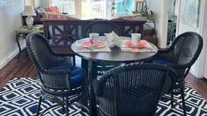 A dining area with wicker chairs, a round table, and a ceiling fan. - Home with beach view from  porch and it’s only a two minute walk to the beach. (Crystal Beach)