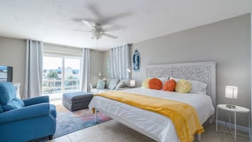 Une chambre d’hôtel moderne avec un grand lit, un fauteuil bleu, une petite table d’appoint et une vue sur la ville grâce à de grandes fenêtres.