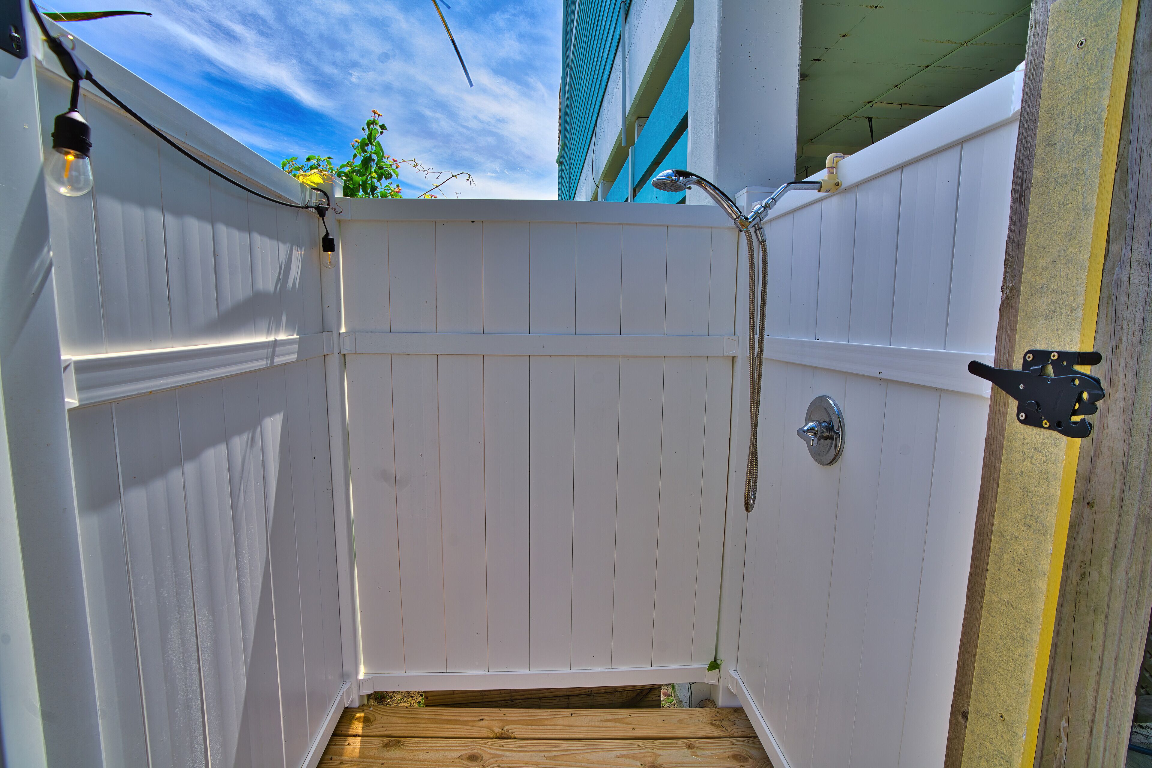 Une cabine de douche extérieure en bois peinte en blanc, dotée d’un plancher en bois, d’une pomme de douche et d’un robinet.