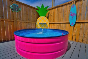 A wooden deck with a pink inflatable hot tub, a pineapple decoration, and a flamingo sign. - Comfy King beds, close to beach, pool + pet friendly (Eastpoint)