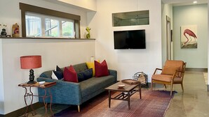 Una sala de estar moderna con un sofá, una mesa de centro y un sillón, un televisor de pantalla plana montado en la pared y un ventilador de techo.