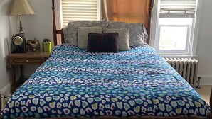 A bedroom with a wooden bed, patterned bedspread, bedside table with lamp, and windows with curtains. - Apt near Temple, St. Christ, Jean, Abington  (Philadelphia)