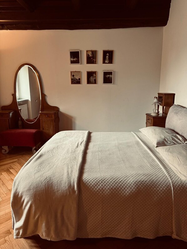 A bedroom with a large bed, a wooden dresser, a mirror, and a wall with framed pictures.